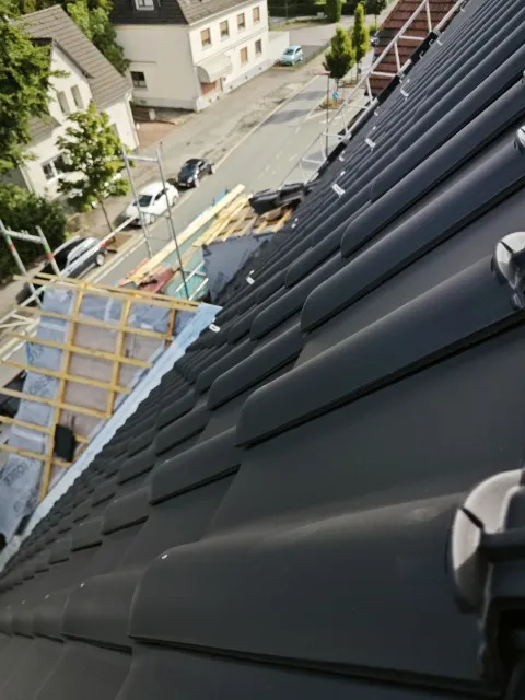 Fast fertig eingedecktes Steildach mit neuen, schwarzen Ziegeln in Nahaufnahme