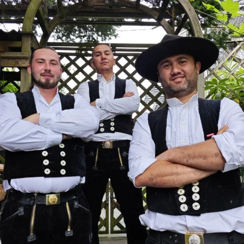 Foto von Zimmerer- und Dachdeckermeister Akbar Venn mit seinen Mitarbeitern in Zunftkleidung auf einer Treppe in einem Garten.