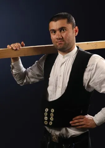 Foto von Zimmerermeister und Dachdeckermeister Akbar Venn in Zunftkleidung mit Holzbalken auf der rechten Schulter